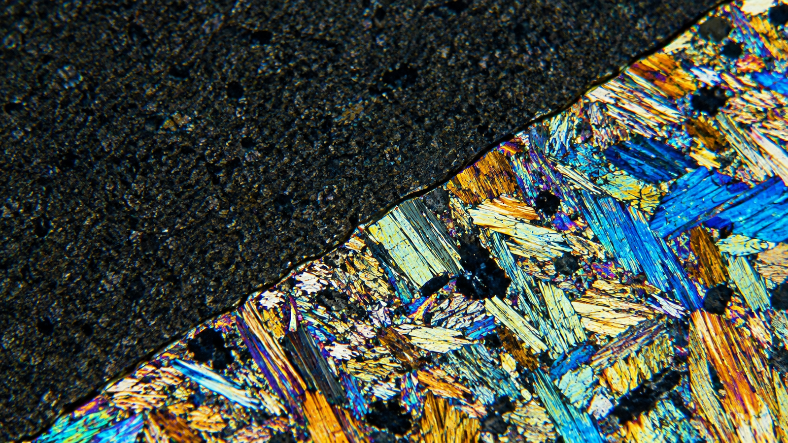 Crystalline sample mid-transformation on a temperature stage with a moving phase front dividing two distinct structures under the microscope