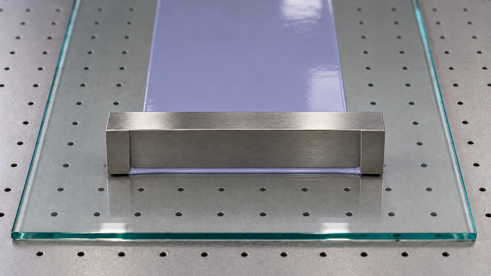 A stainless steel film applicator blade drawing a smooth wet film across a glass plate on a vacuum panel, with a small bead of liquid in front of the blade