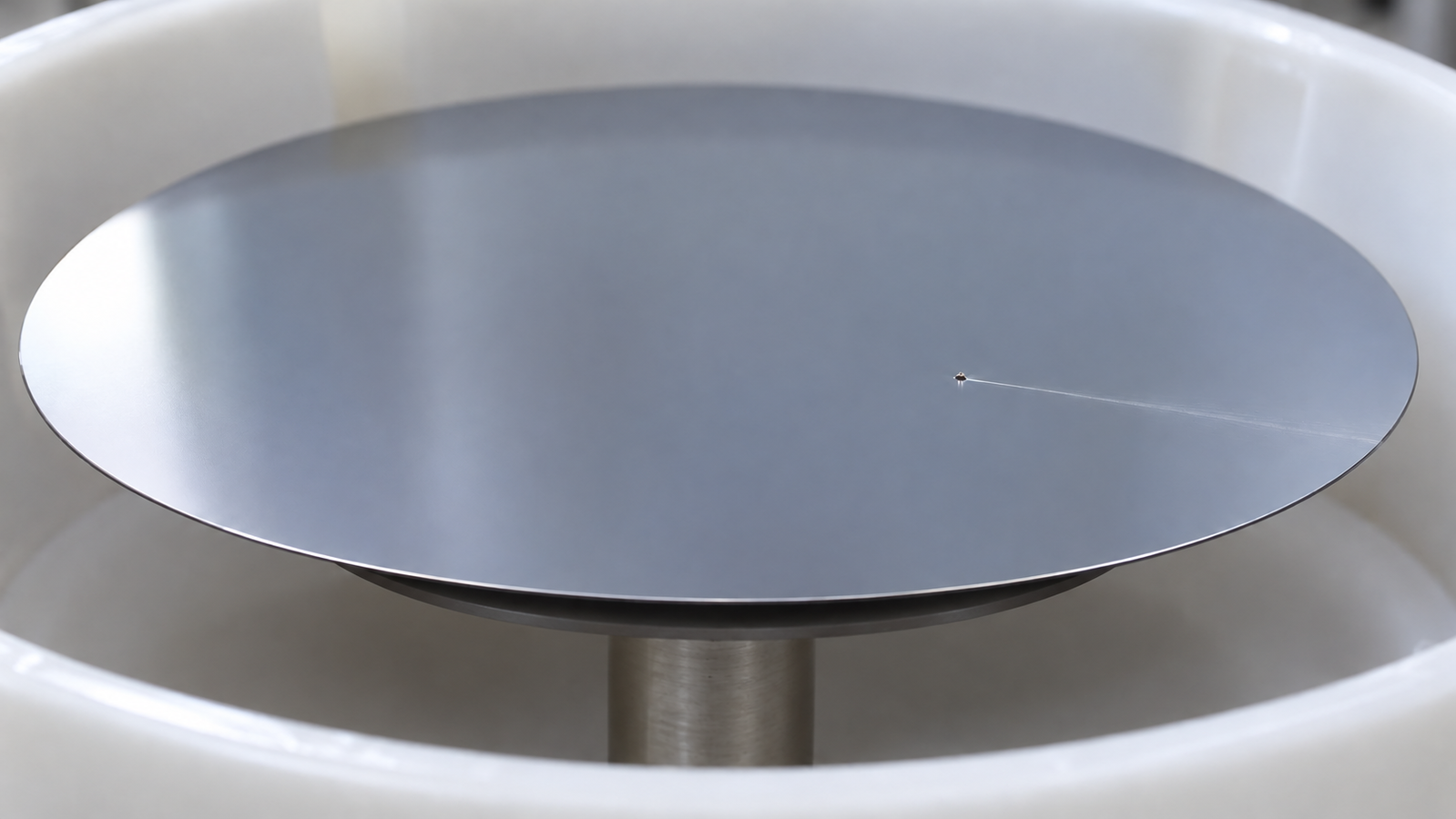 Close-up of a coated silicon wafer under raking light on a spin coater chuck, with a single fine comet streak running outwards from a tiny particle