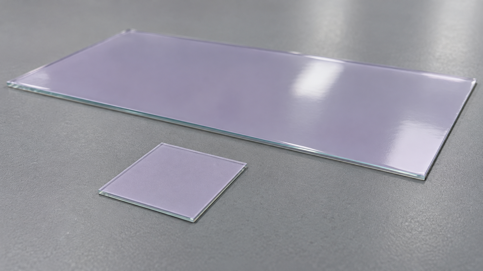 A small coated square glass substrate beside a larger glass plate with a uniform wet film, on a plain laboratory bench